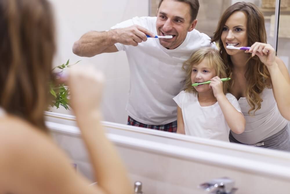 Family of three brushing their teeth and looking in a mirror