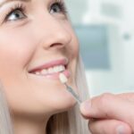 Dental veneer held up to a woman's teeth