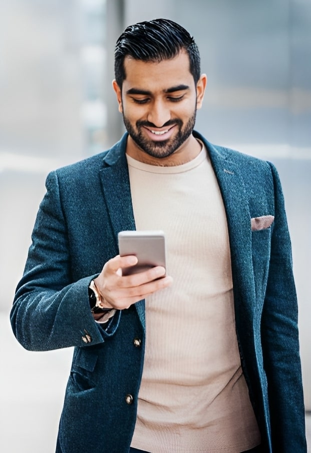 A young man dressed in a suit smiling while looking at his cell phone